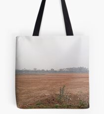 A wide open dusty field surrounded by cars, trees and buildings Tote Bag